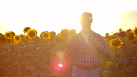 A-young-farmer-in-plaid-shirt-and-jeans-uses-VR-glasses-on-the-field-with-sunflowers-for-scientific-article.-These-are-modern-technologies-in-summer-evening.